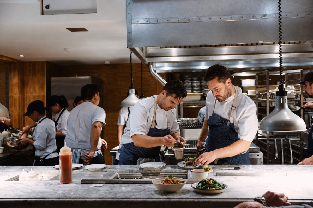 Chefs plating dishes together in an open restaurant kitchen