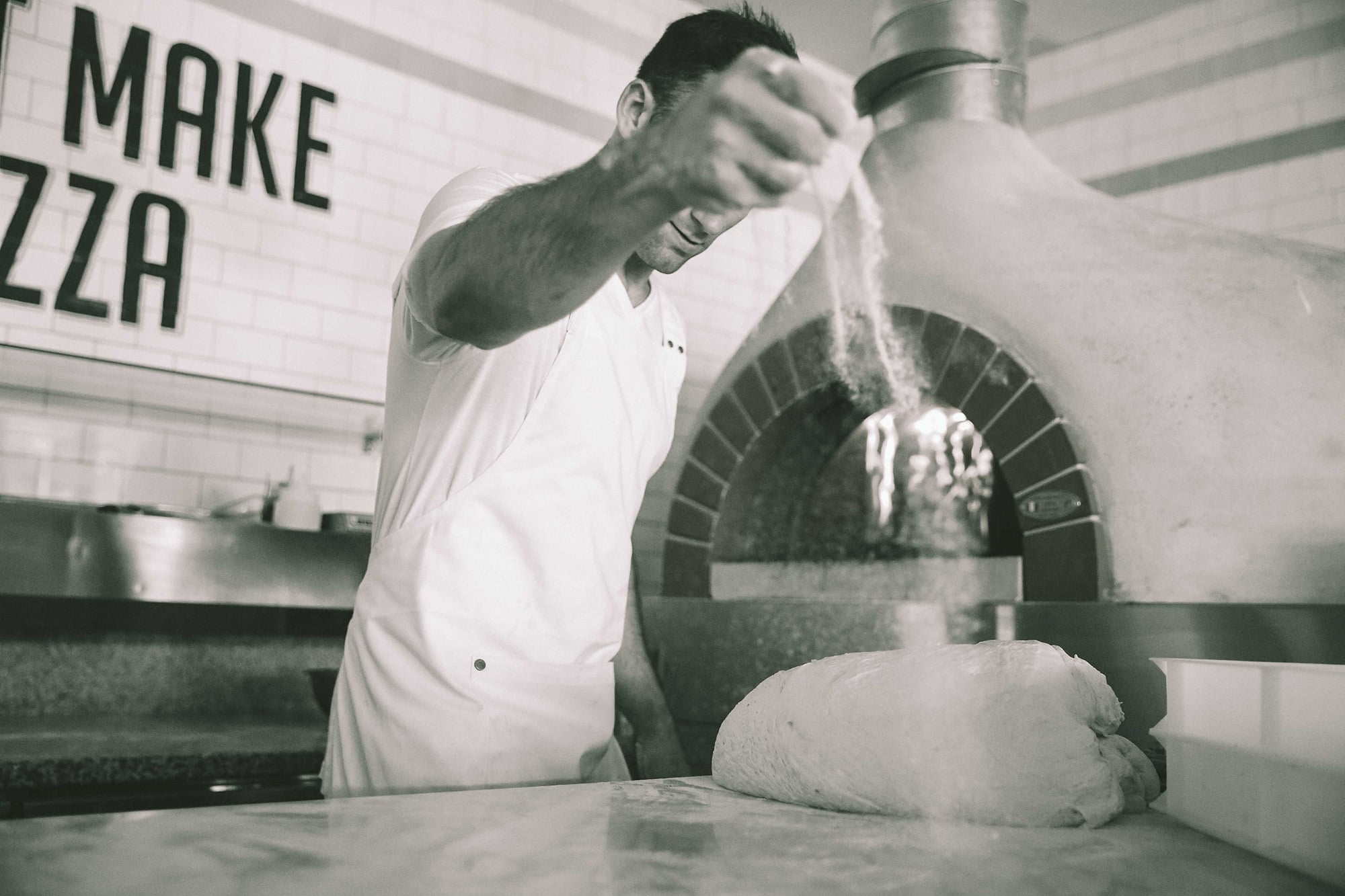 Chef stretching pizza dough at a wood-fired oven