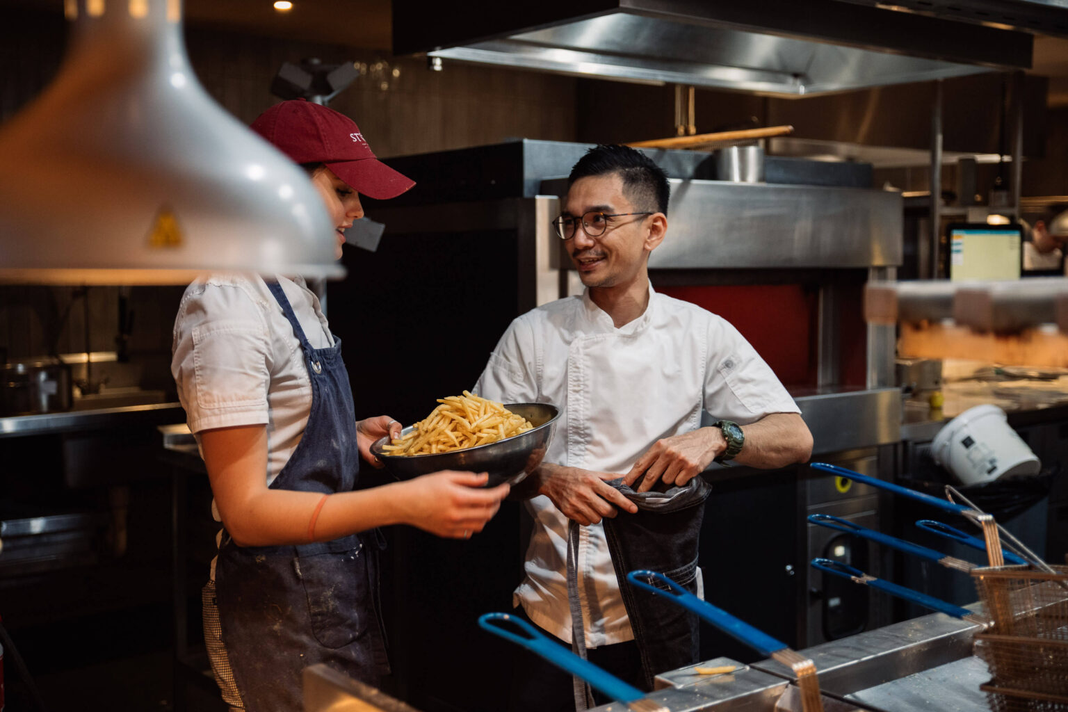 Two chefs serving plates in a busy kitchen